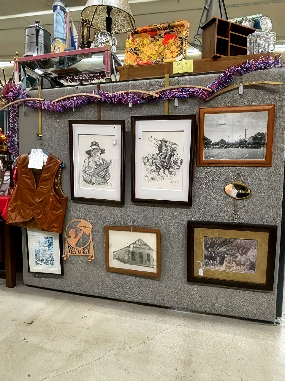 Framed pencil drawings and old photographs on a booth wall beside a vest on a hanger